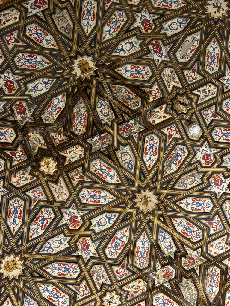 A carved wooden ceiling of interlocking twelve-pointed stars, each panel painted with red and blue scrollwork.