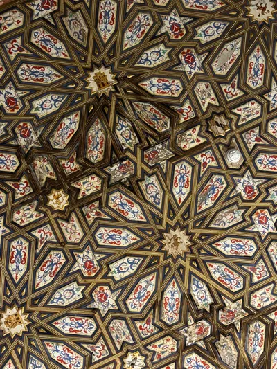 A carved wooden ceiling of interlocking twelve-pointed stars, each panel painted with red and blue scrollwork.
