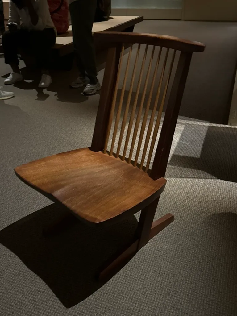 A walnut chair with a thick sculpted seat, a row of thin spindles in the back, and a cantilevered base resting on two runners.