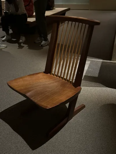 A walnut chair with a thick sculpted seat, a row of thin spindles in the back, and a cantilevered base resting on two runners.